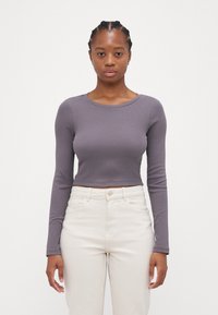Long-sleeve, cropped top in muted gray ribbed fabric, featuring a round neckline. Paired with light-colored high-waisted jeans.