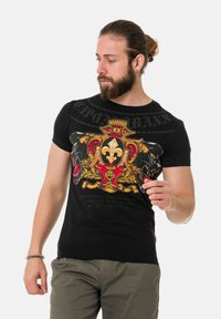 Schwarzes T-Shirt mit kurzen Ärmeln, das ein farbenfrohes Wappen-Design mit goldenen und roten Akzenten, Panthergrafiken und fettem Text zeigt.