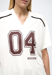 Maillot de sport blanc avec encolure en V, manches courtes et tissu texturé. Comprend un grand imprimé "04" marron et le logo "MODSTRÖM".