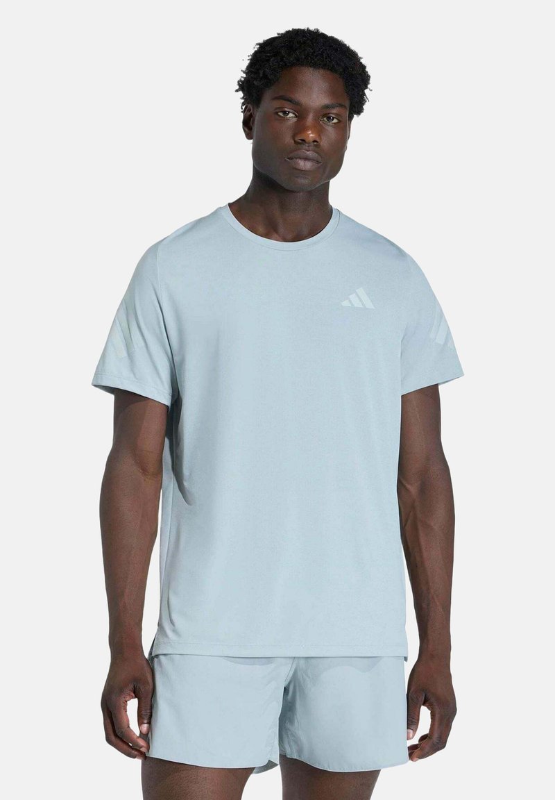 Homme portant un t-shirt de sport bleu clair et un short assorti, debout devant un fond blanc uni.