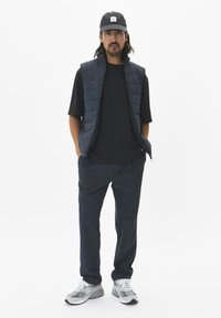 Navy puffer vest over a black t-shirt, paired with dark pants and grey sneakers. The cap is navy with a white label. Minimalist design.