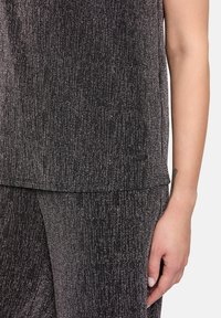Outfit in tessuto nero e grigio con linee verticali sottili; presenta una vestibilità rilassata, maniche corte e un piccolo dettaglio con logo.
