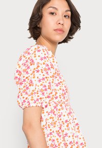 Vestido floral branco com padrões de flores em rosa e laranja, mangas curtas bufantes, corpete franzido e um corte relaxado. Textura de tecido suave.
