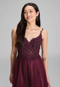 Burgundowa suknia z koralikowym i kwiatowym haftem na górze, z cienkimi ramiączkami i zwiewną tiulową spódnicą. Gładki, teksturowany materiał.