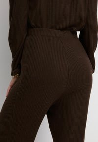 Leggings marrones de canalé con una cintura alta, que presentan una textura vertical y sutilezas de costura en la parte posterior para un ajuste ceñido.