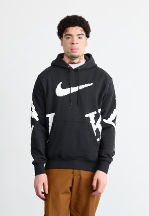 Crna dukserica s bijelim Nike logoom i oversized natpisom. Ima kenguru džep i kapuljaču s vezicom. Mekani pamučni materijal.