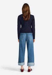 Navy long-sleeve top paired with light blue, wide-leg jeans featuring turned-up cuffs. Footwear is red, glossy shoes.