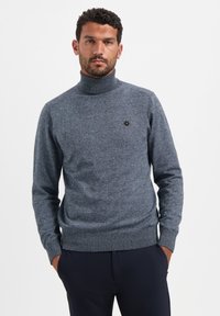 Grijze, getextureerde coltrui met lange mouwen en een aansluitende zoom. Bevat een klein logo op de borst en een gladde hals.