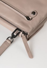 Beige Leder Umhängetasche mit einem Reißverschluss, ausgestattet mit schwarzem Beschlag, einem abnehmbaren Schulterriemen und subtilen Stichdetails.