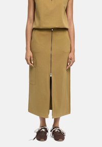 Oliwkowa, fakturowana bawełniana spódnica z przednim zamkiem, bocznymi kieszeniami i prostym krojem, zestawiona z brązowymi sneakersami i sznurówkami.