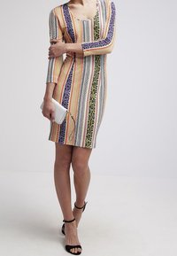 Flerfärgad klänning med lång ärm som har randiga mönster med ormskinn och geometriska design, kombinerad med en silverfärgad klutch och svarta sandaler.