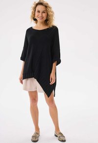 Czarny, oversize sweter dzianinowy z rękawami o długości trzech czwartych, teksturowanym diagonalnym wzorem i prążkowanym dołem, w zestawie z beżowymi szortami i wzorzystymi butami.