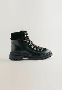 Botte de randonnée en cuir noir et en daim avec œillets en métal et empiècements de textures variées, dotée d'une semelle en caoutchouc épaisse avec des crampons profonds.