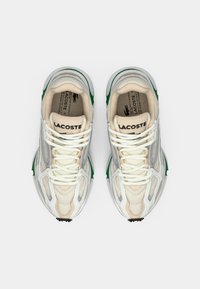 Ett par beige och vita Lacoste-sneakers med gröna detaljer sedda uppifrån på en vit bakgrund.