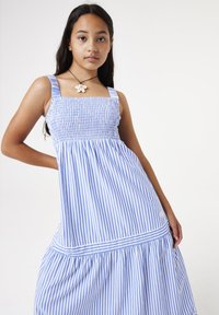 Ein blau-weiß gestreiftes Sommerkleid mit gesmocktem Oberteil, breiten Trägern und einem gestuften Rock. Es verfügt über ein weißes horizontales Band in der Taille.