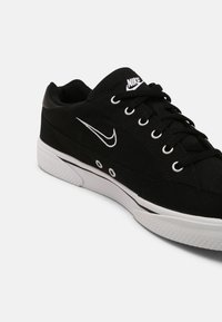 Svarta canvas sneakers med vita detaljer, som har en klassisk design, rund tå, snörning och en texturerad gummisula.