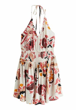 Robe d'été blanche à motif floral avec un corsage ajusté, une jupe évasée et des bretelles réglables. Portée avec des sandales foncées ornées de clous.