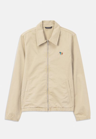 Beige zip-up jacka med spetsig krage, två framfickor, elastiska ärmslut och nederkant, samt en liten flerfärgad broderad häst på bröstet.