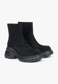 Black suede ankle boots with a chunky rubber sole, featuring a smooth texture and rounded toe, designed with elastic side panels for easy wear.