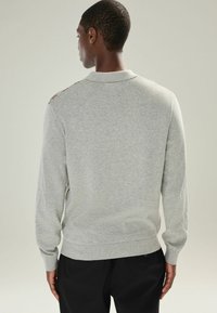 Grå sweater med krave og lange ærmer, der har en glat tekstur og subtile detaljer på skuldrene.