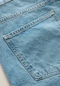 Detailní záběr na světle modrou džínovinu ukazující zadní kapsu s viditelným prošitím a vybledlou strukturou.
