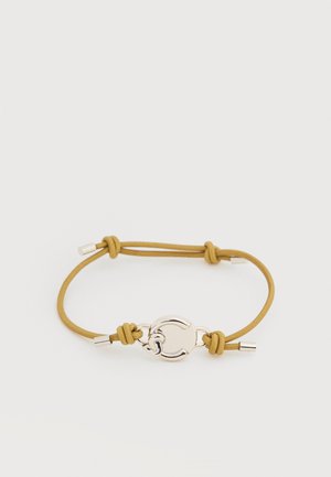 Bracelet en corde moutarde ajustable avec une fermeture ronde en argent et des embouts métalliques, posé à plat sur une surface blanche.