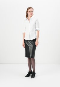 Camicia bianca con maniche arrotolate, gonna nera in pelle a tubino, collant trasparenti neri e stivali neri a punta con dettagli in pizzo.