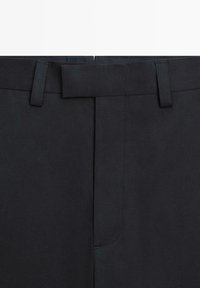 Primo piano della vita di pantaloni neri con passanti per cintura e chiusura anteriore nascosta.