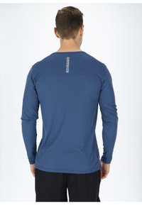 Camicia a maniche lunghe di colore blu scuro, in tessuto leggero e texture, con colletto rotondo e dettaglio logo sulla parte superiore della schiena. Design semplice e aderente.