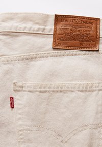 Lichtbeige denim jeans met een leren patch met geperst merklogo, een rode label aan de zijkant en tonale stikdetails.
