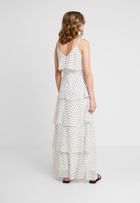 Vestido maxi blanco con lunares negros, con volantes en capas, tirantes de espagueti ajustables y un diseño de espalda en forma de V.