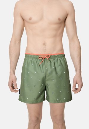Bañador verde con pequeños estampados de pingüinos blancos, cintura y cordón color coral naranja, usado por un hombre sin camiseta desde la mitad del muslo hacia arriba.