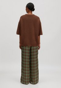 Brauner, gestrickter Oversize-Pullover mit kurzen Ärmeln, kombiniert mit lockeren, grünen Karohosen mit orangefarbenen und blauen Akzenten.