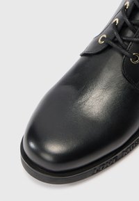 Must musta nahkasaapad sileda viimistlusega, ümarate varvastega, kuldsete aasadest ja mustade paeltest. Tekstuuriga talla peal on embosseeritud "LOVE MOSCHINO" detail.