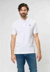 White short-sleeve polo shirt with a two-button placket and a small navy logo on the chest. Worn with blue denim jeans.
