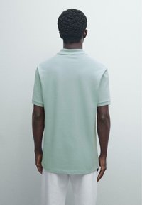 Ljusgrön pikétröja i mjukt tyg, med klassisk krage, korta ärmar och avspänd passform, bärs med vita byxor.