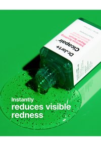 Klart grønt gelé i en gjennomsiktig flaske, vippet over. Hvitt merke viser produktnavn og fordeler. Gelé samlet på en grønn overflate.