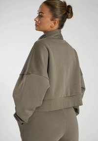 Khaki cropped sweatshirt met een hoge kraag, drop shoulders, ribbelrand en een zachte textuur. Het ontwerp heeft minimale stiksels en geen zichtbare logo's.