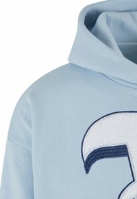 Light blue hooded sweatshirt with ribbed texture, featuring a large white and navy embroidered logo on the front.