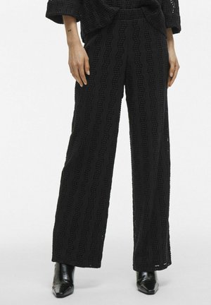 Black wide-leg pants featuring a textured fabric with a wavy pattern. They are detailed with a high waistband and slightly cropped length.