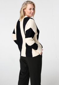 Grofgebreide trui met zwarte en crèmekleurige diagonale strepen, een losse pasvorm en een geribde zoom, gedragen over een zwarte broek.