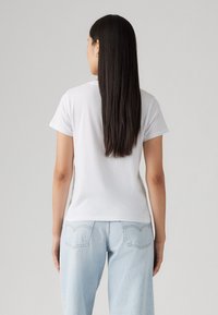 Hvit t-skjorte med kort erme og rund hals, satt sammen med lyseblå denim jeans med baklommer og slitt vask.