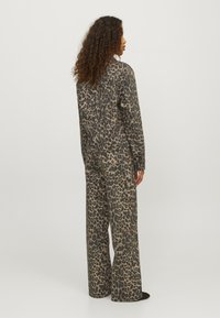 Leopard print jumpsuit in beige and black. Features long sleeves, wide legs, and a relaxed fit. Material has a smooth texture.