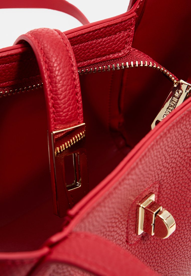 Sac à main en cuir texturé rouge avec une poche zippée, des accents en métal doré et une forme structurée. La vue intérieure met en valeur la doublure et les détails.
