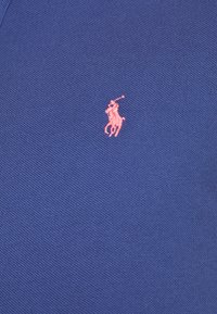 Mörkblå pikétröja med texturerad tyg och en liten rosa broderad logotyp av en pony på vänster bröst.