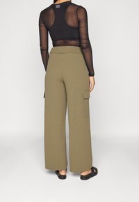 Khaki cargobroek met een elastische tailleband, wijde benen, zijvakken en een gladde textuur, gecombineerd met een doorzichtig zwart langemouwen top.