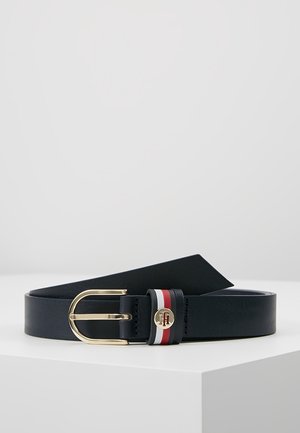Ceinture en cuir noir avec une boucle dorée et une boucle rayée rouge, blanche et noire ornée d'un petit logo doré, posée sur une surface blanche.