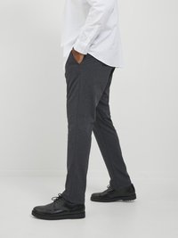 Pantalones grises de diseño ajustado, fabricados con una tela suave de textura lisa. Combinados con zapatos de cuero negros con cordones redondos.