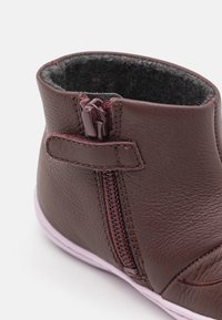 Botín de cuero marrón con cierre de cremallera y un interior suave y texturizado. Punta redondeada y suela de goma rosa. Diseño compacto sin adornos.