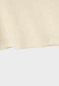 Kremasto obarvan rebrast tekstil z vidnim šivanjem vzdolž ukrivljenega roba na nevtralnem ozadju.